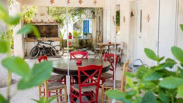 A patio with a round table and red chairs, a bicycle, and a brick oven.