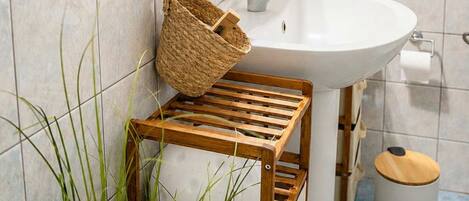 A bathroom with a white sink, a mirror, a towel rack, a trash bin, and a small window.