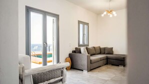 Una sala de estar con un sofá gris, un sillón blanco y un ventanal con vista al mar.