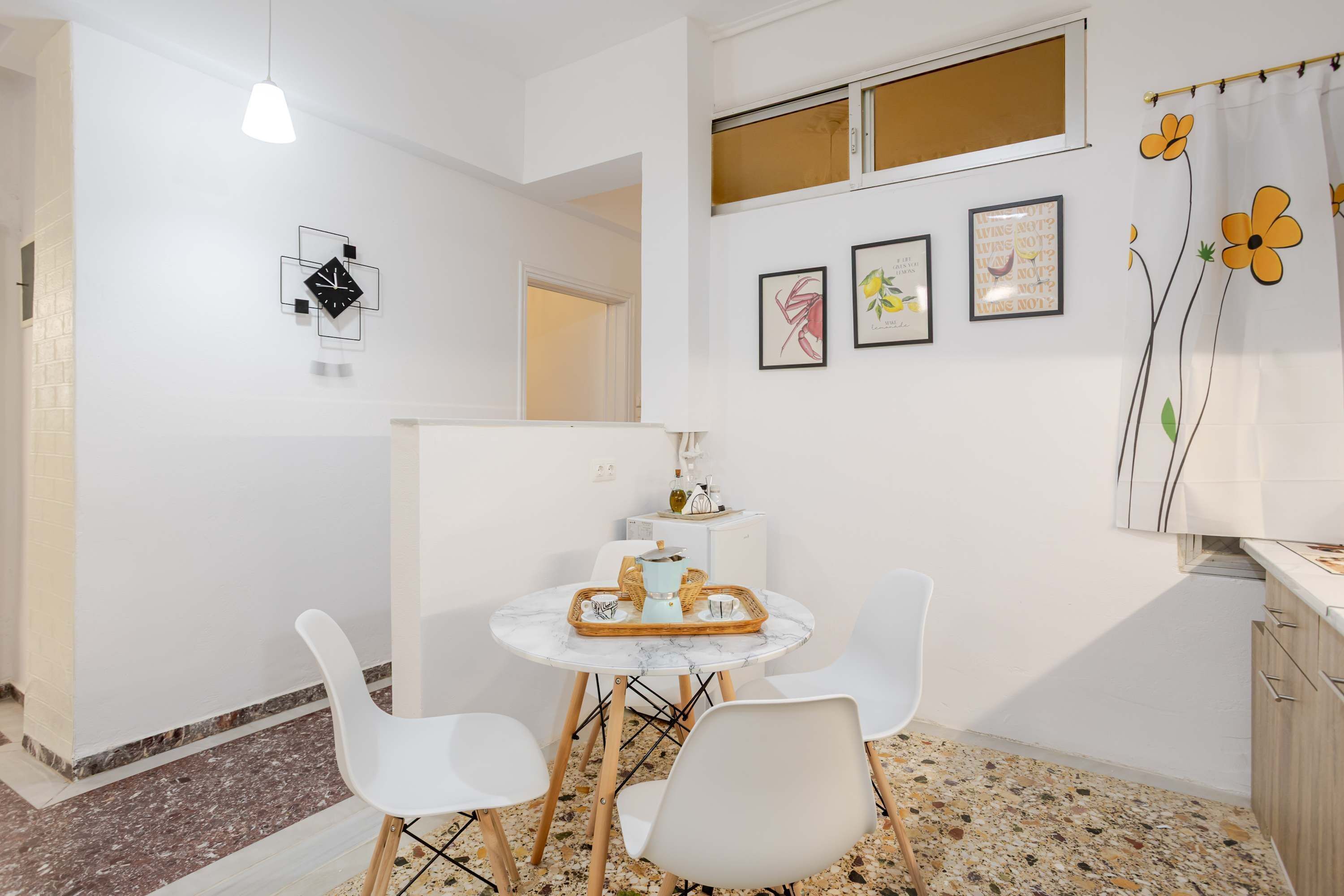 Una cocina moderna con armarios blancos, una mesa de comedor con sillas y una pared decorativa con obras de arte enmarcadas.