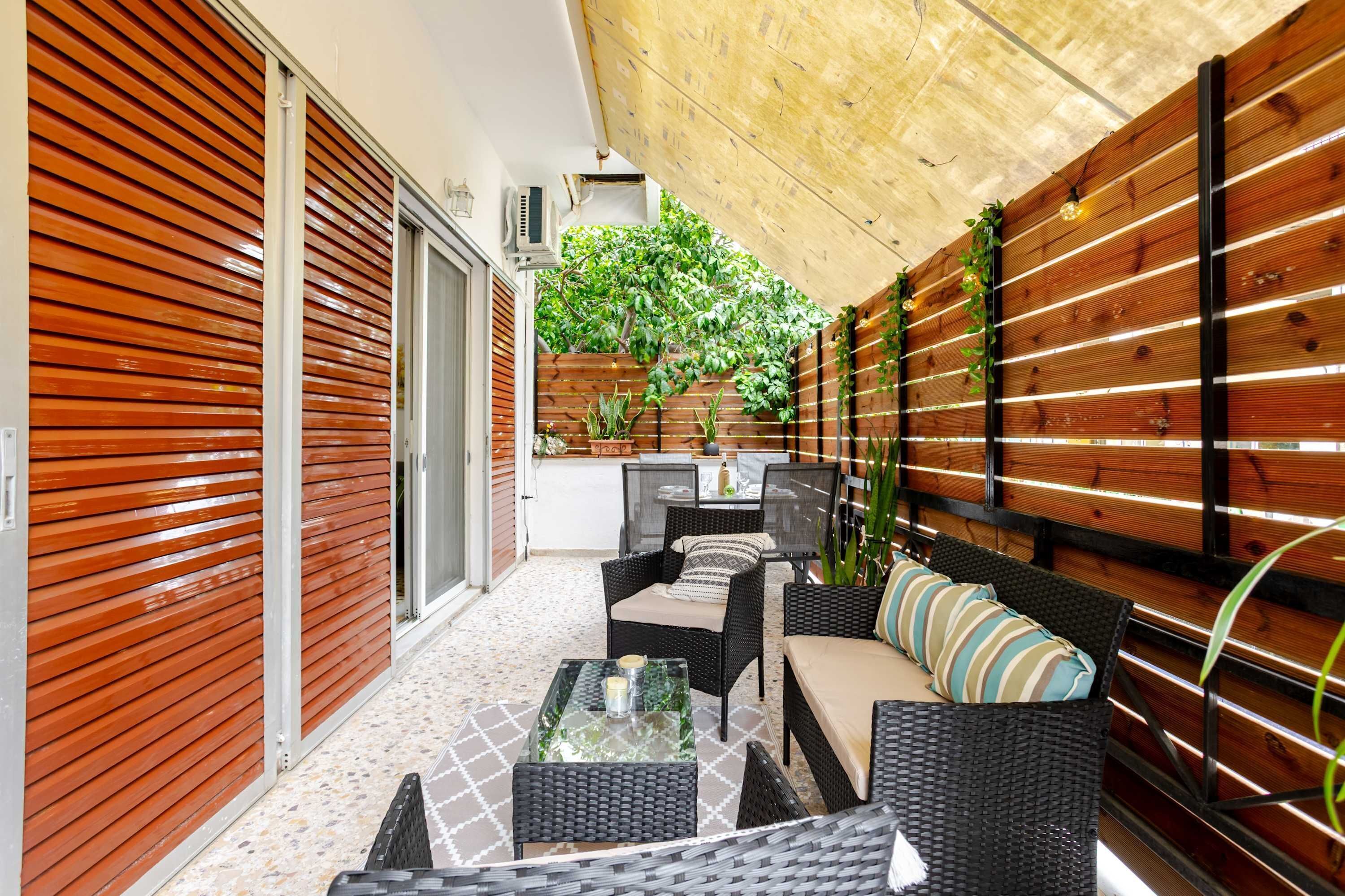 Eine Terrasse mit Korbmöbeln, einem Glastisch und einem Holzzaun mit Pflanzen.