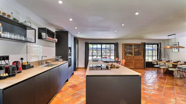 A modern kitchen with a central island, built-in appliances, and a dining area with a table and chairs. - L'écrin d'été - Nature & Calm (Ventabren)
