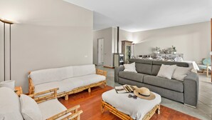 A living room with a sofa, a couch, and a wicker chair. There is a dining table with chairs in the background. - Riflessi Di Luce: Lake Maggiore View Balcony Stresa (Stresa)