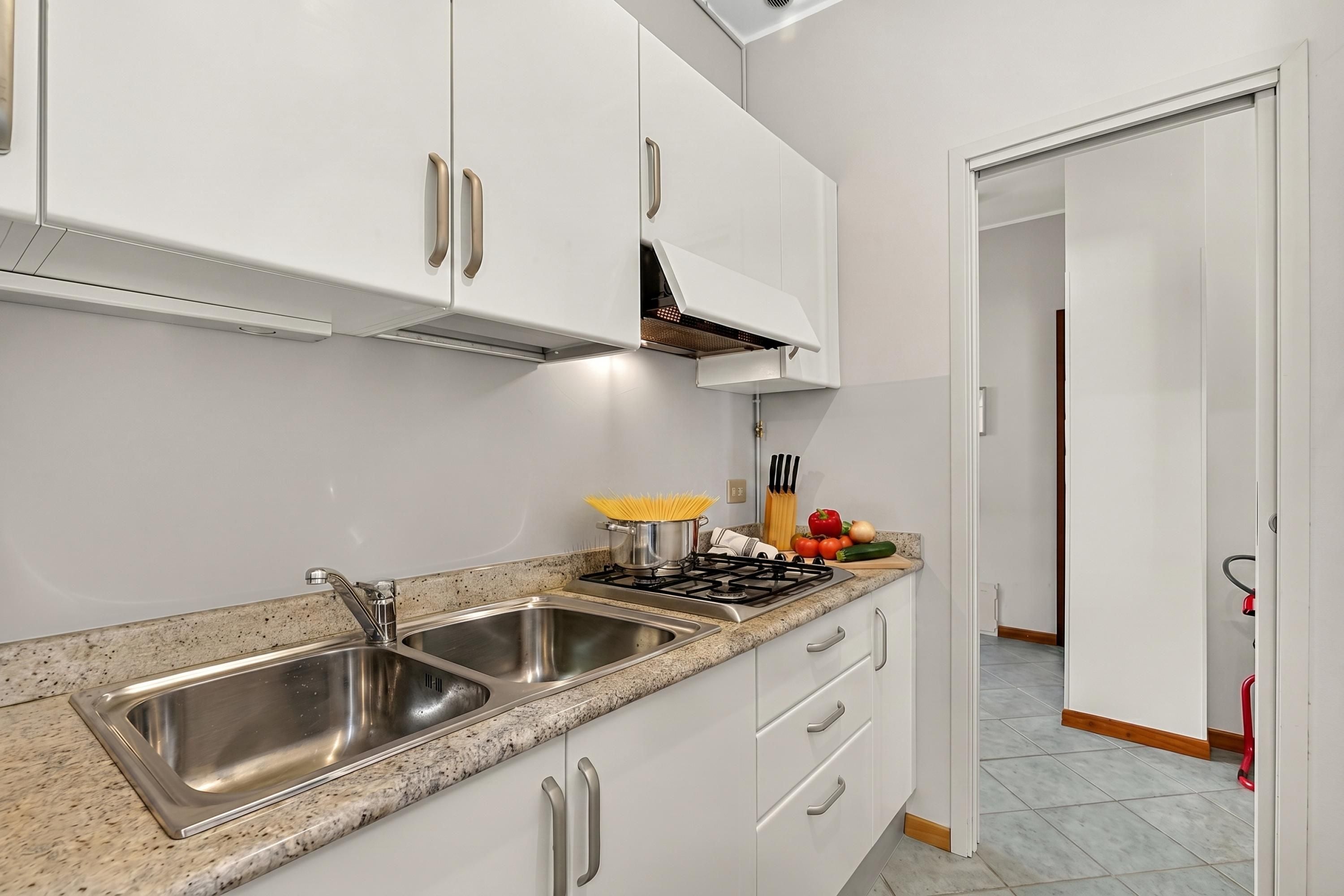 A kitchen with stainless steel sinks, white cabinets, a gas stove, and a countertop with various kitchen items.