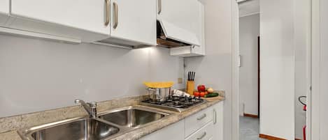 A kitchen with stainless steel sinks, white cabinets, a gas stove, and a countertop with various kitchen items.