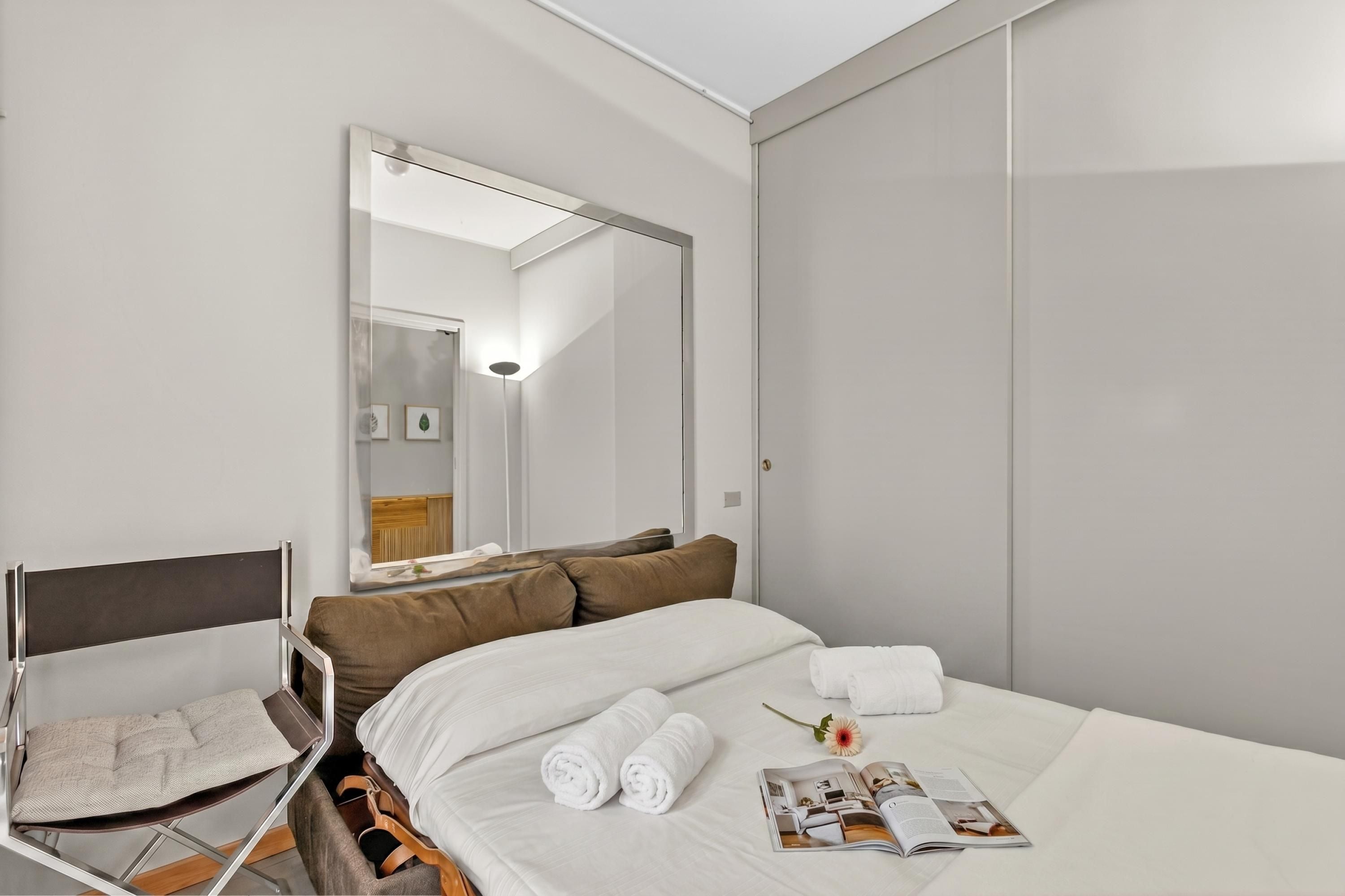 Ein Hotelzimmer mit Bett, Stuhl, Spiegel und Kleiderschrank.