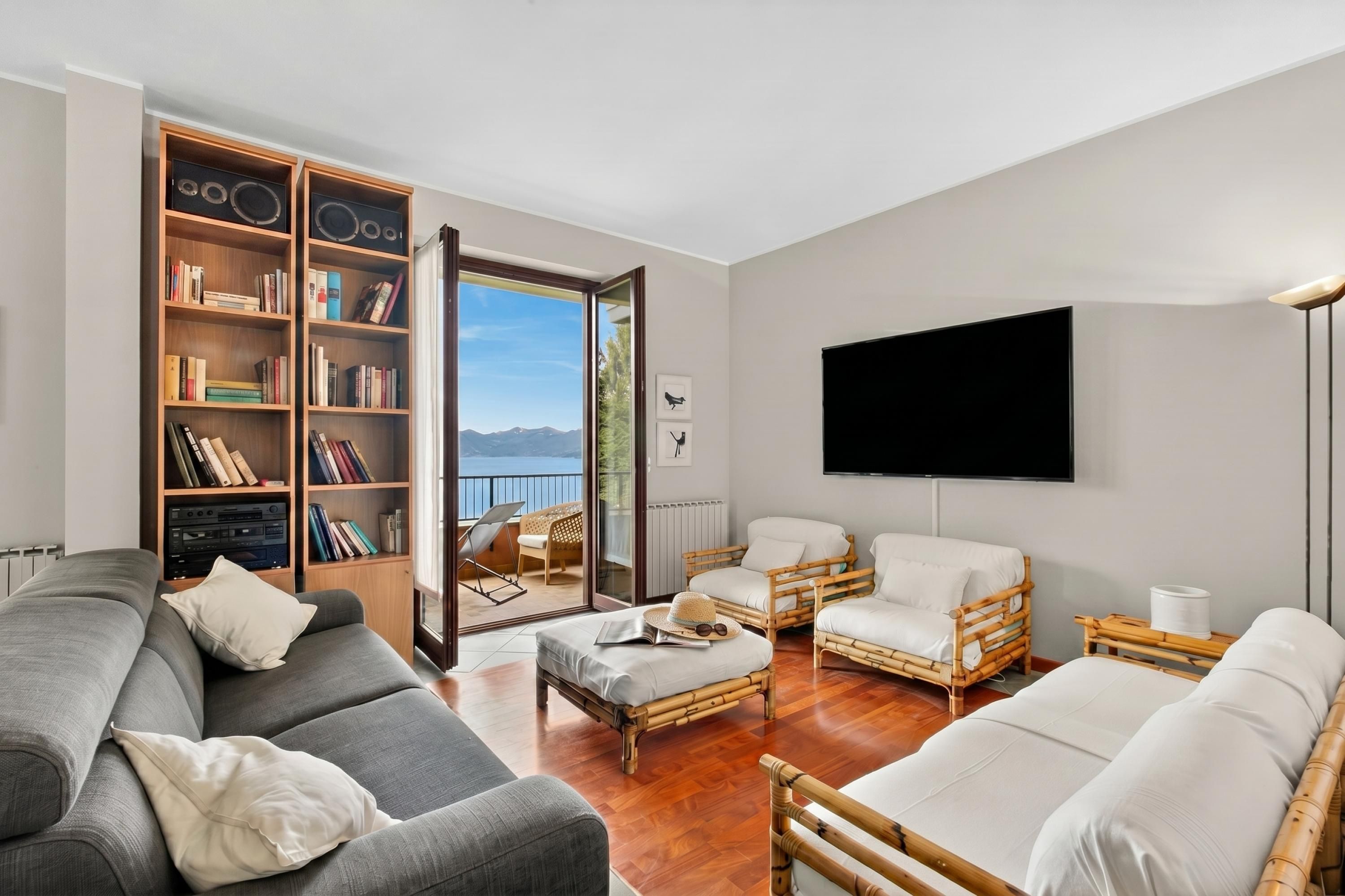 A living room with a sofa, two armchairs, a flat-screen TV, a bookshelf, and a view of the outdoors.