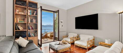 A living room with a sofa, two armchairs, a flat-screen TV, a bookshelf, and a view of the outdoors.