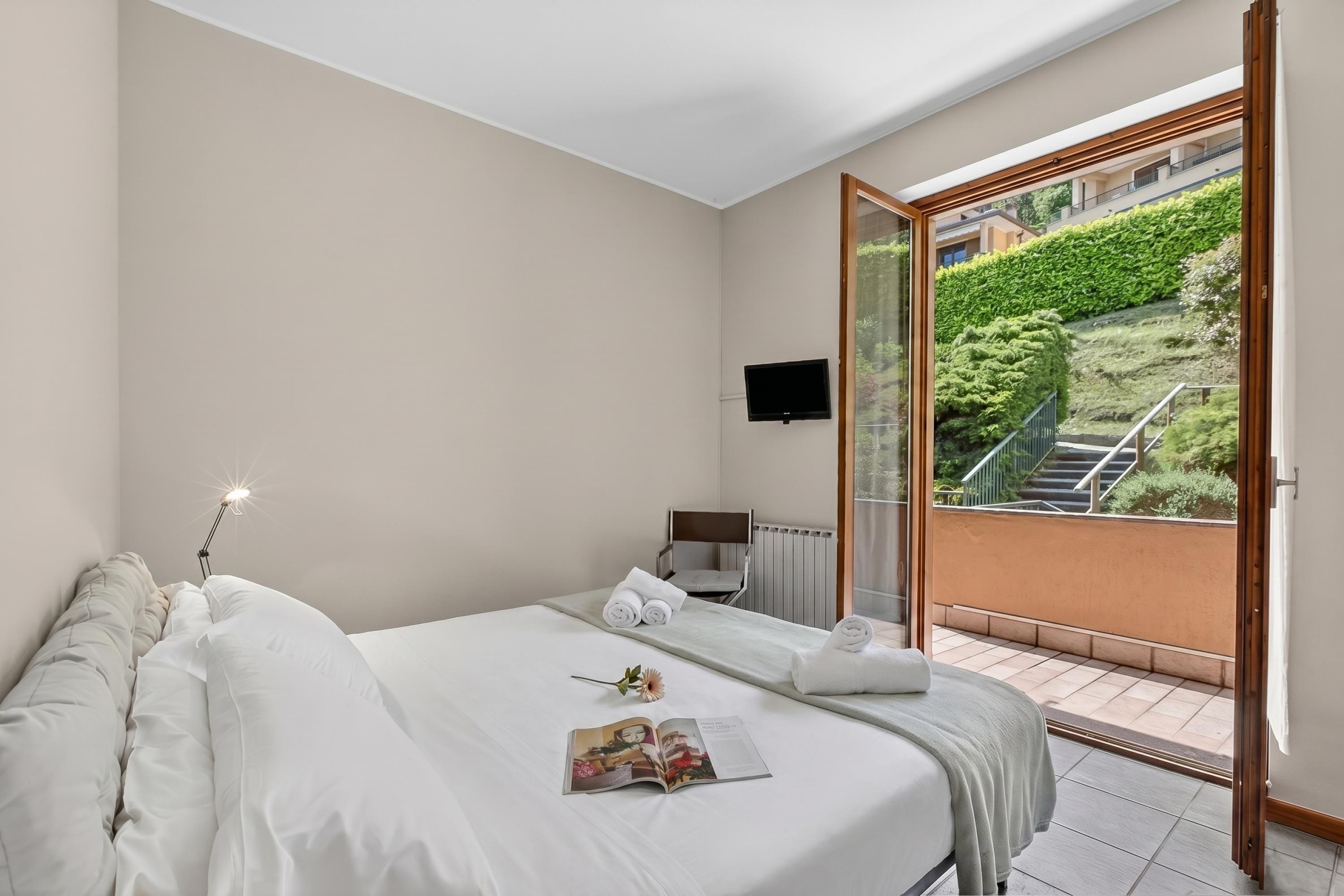 Hotelkamer met een bed, nachtkastje, televisie en uitzicht op een tuin en een buitentrap.