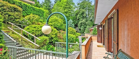 Un balcón con banca de madera, baranda de metal y una escalera que lleva a un edificio con techo verde.