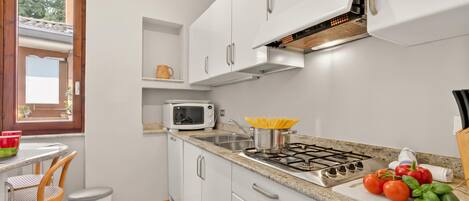 A modern kitchen with white cabinets, a microwave, a gas stove, and a window.
