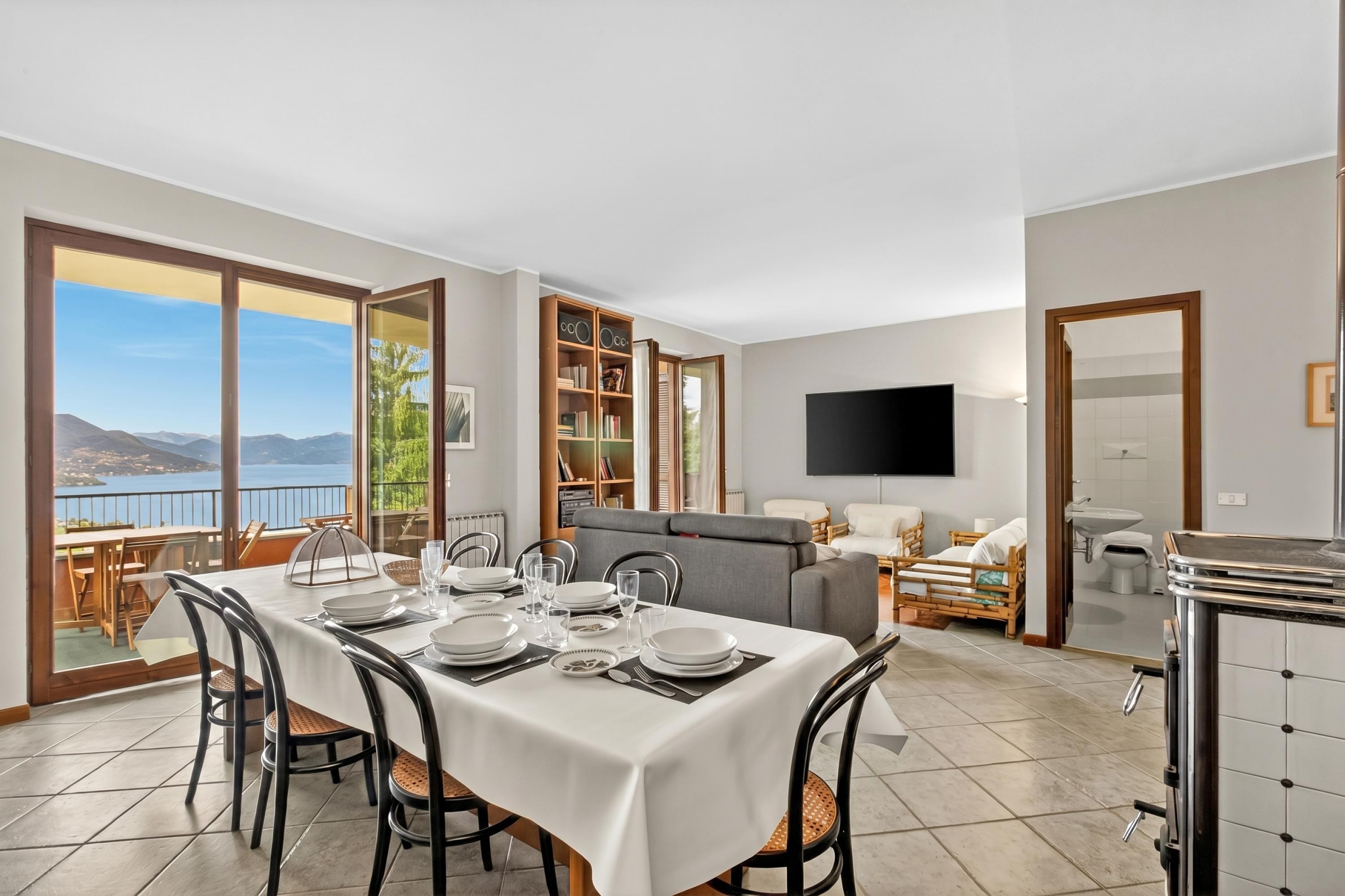 Un coin repas avec une table dressée pour quatre personnes, un canapé, un téléviseur et une vue sur les montagnes.