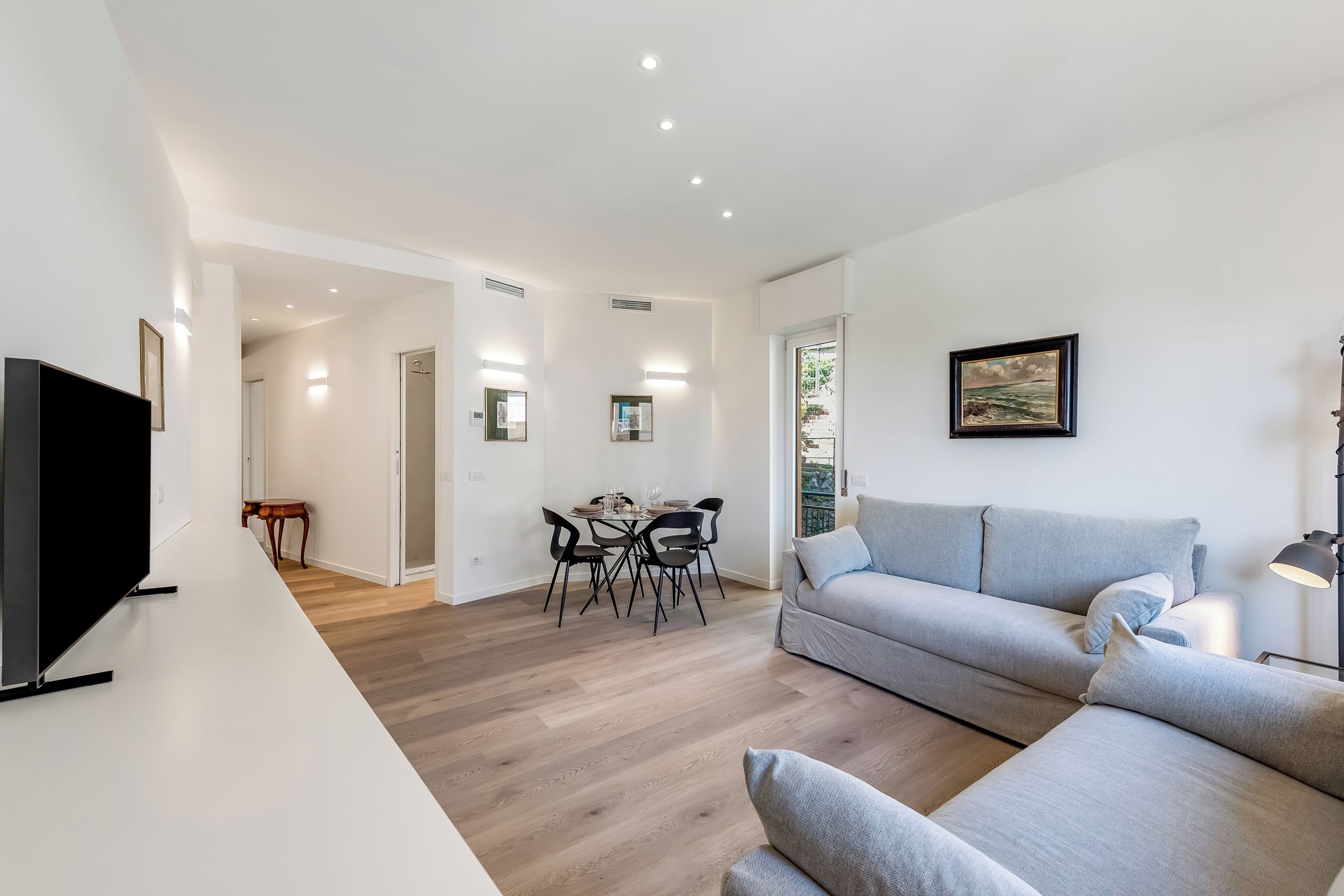 A modern living room with a grey sofa, a flat-screen TV, and a dining area with a table and chairs.