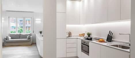 Una cocina moderna con armarios blancos, horno empotrado y pileta de acero inoxidable.