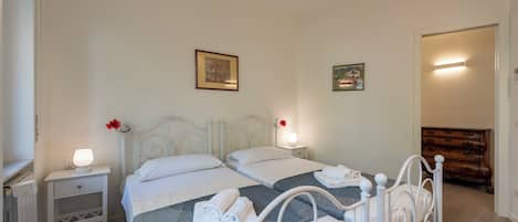 A bedroom with two beds, white headboards, bedside tables with lamps, and a dresser.