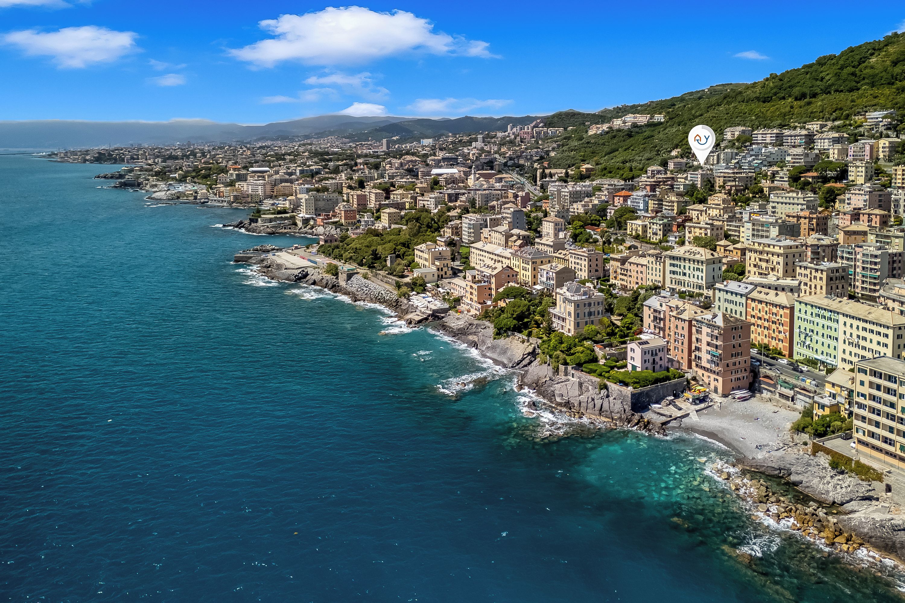 Un paysage urbain côtier avec des bâtiments le long du front de mer, un ciel dégagé et une chaîne de montagnes en arrière-plan.