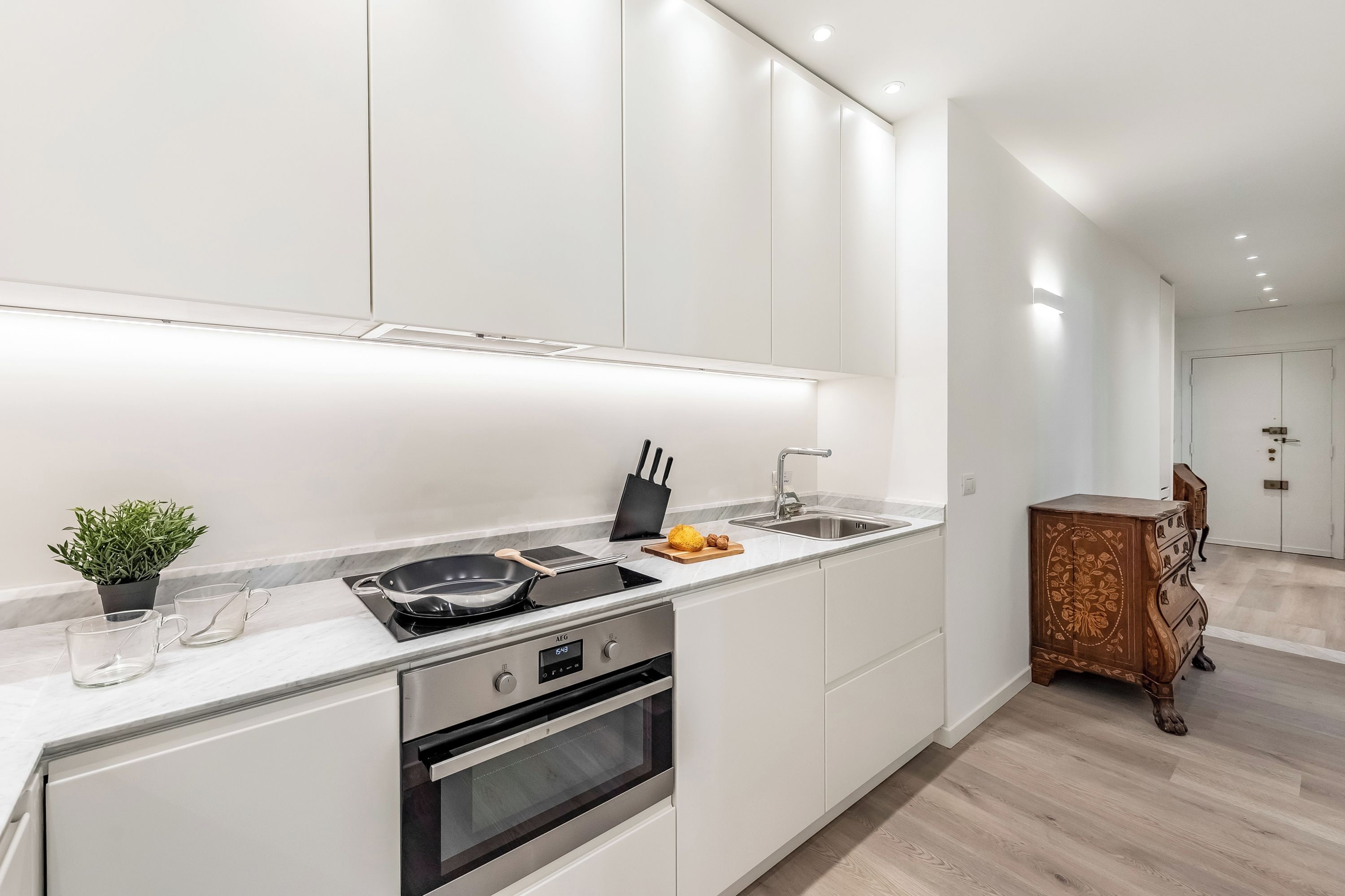 A modern kitchen with white cabinetry, a built-in stove, oven, and a wooden sideboard.