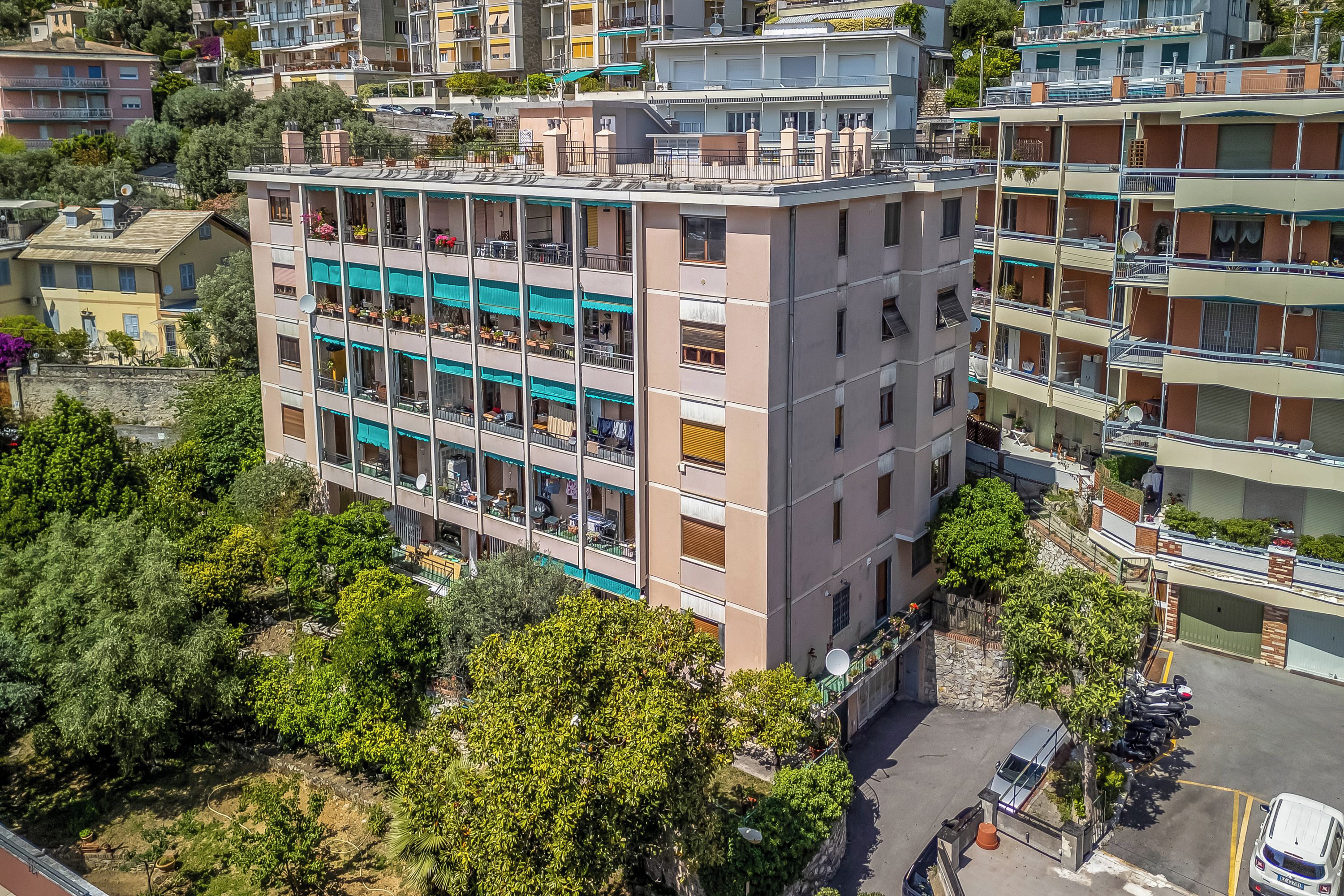 Un edifici de diverses plantes amb balcons, una zona d'aparcament i vegetació als voltants.