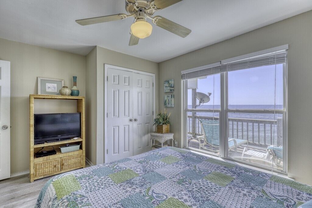 Ein Schlafzimmer mit Bett, Fernseher auf einem Holzboden, einer Tür und einem Balkon mit Meerblick.