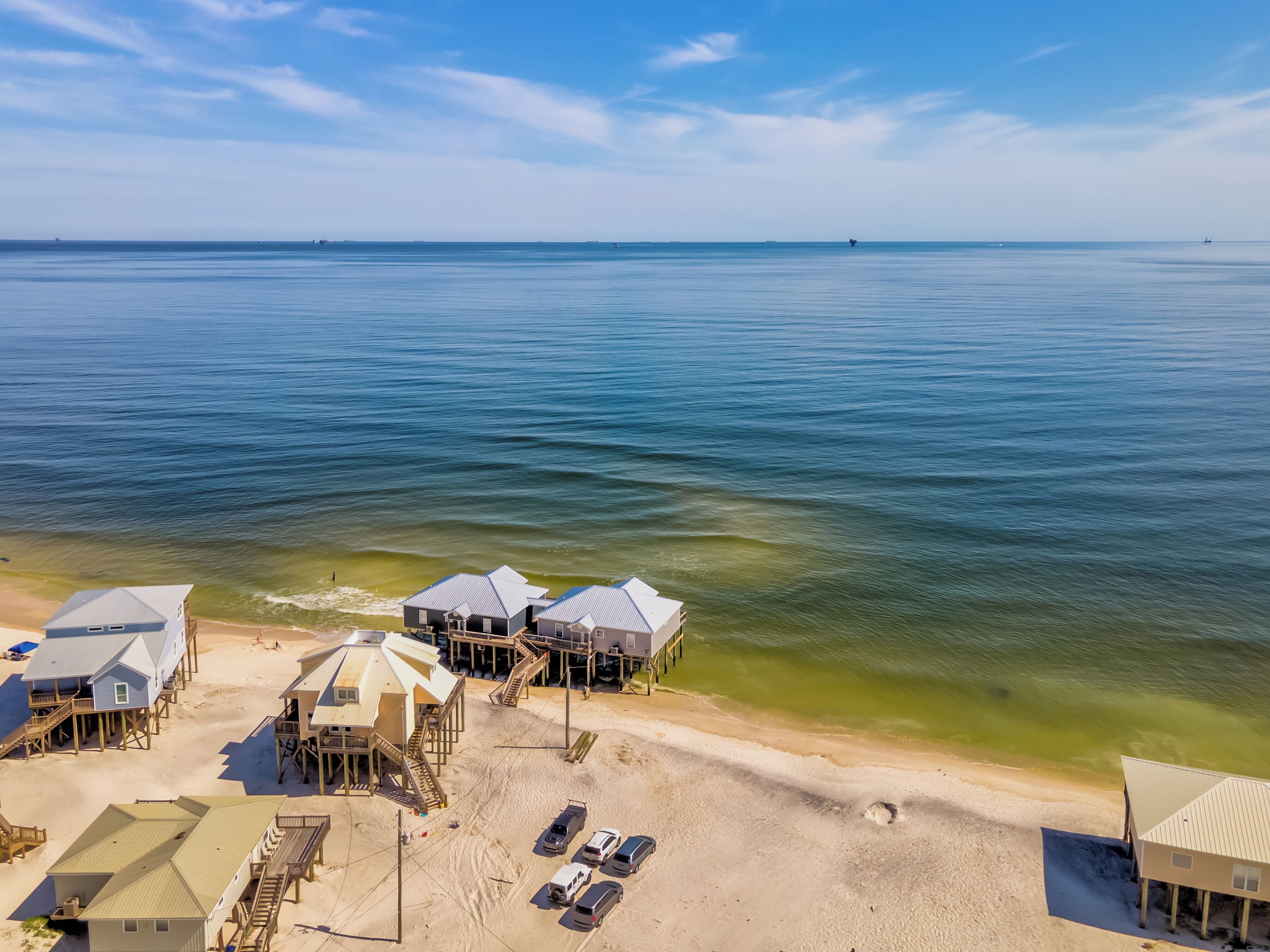 A beachfront property with multiple buildings, a sandy beach, and a clear view of the ocean.