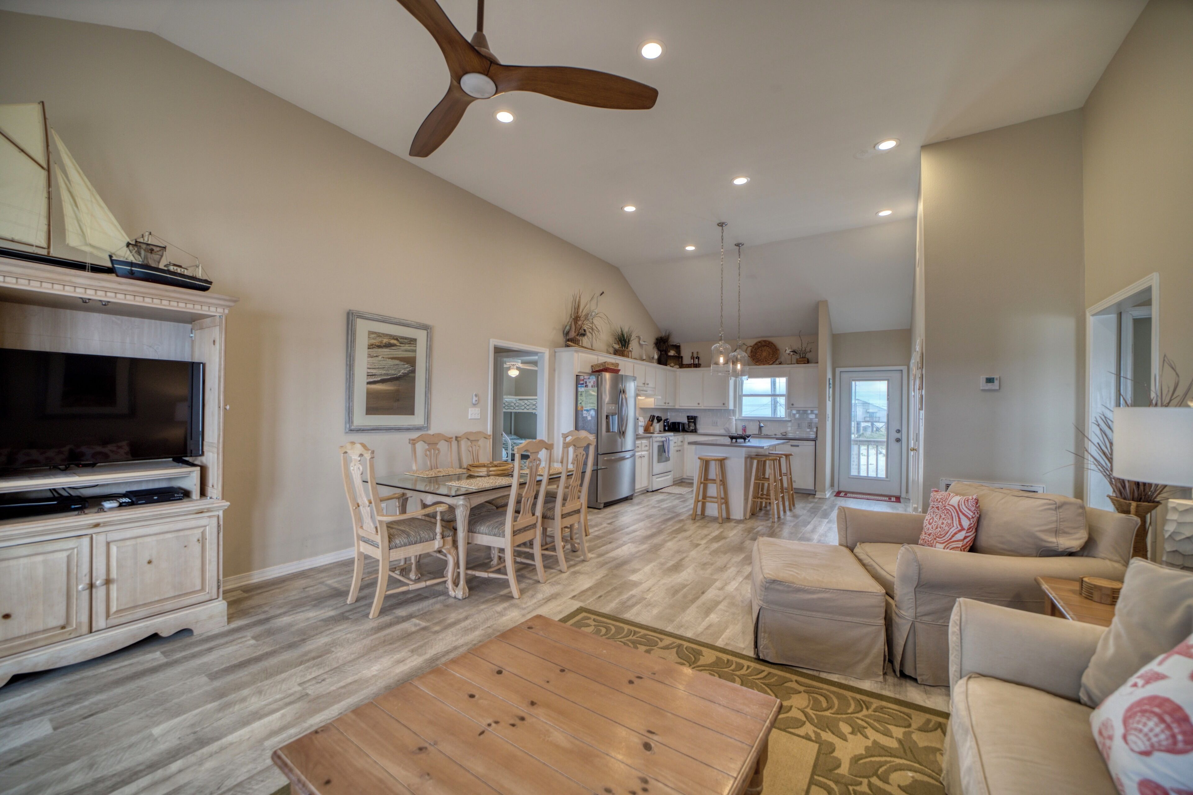 Un salon spacieux avec une table basse en bois, des canapés de couleur beige et un ventilateur de plafond.