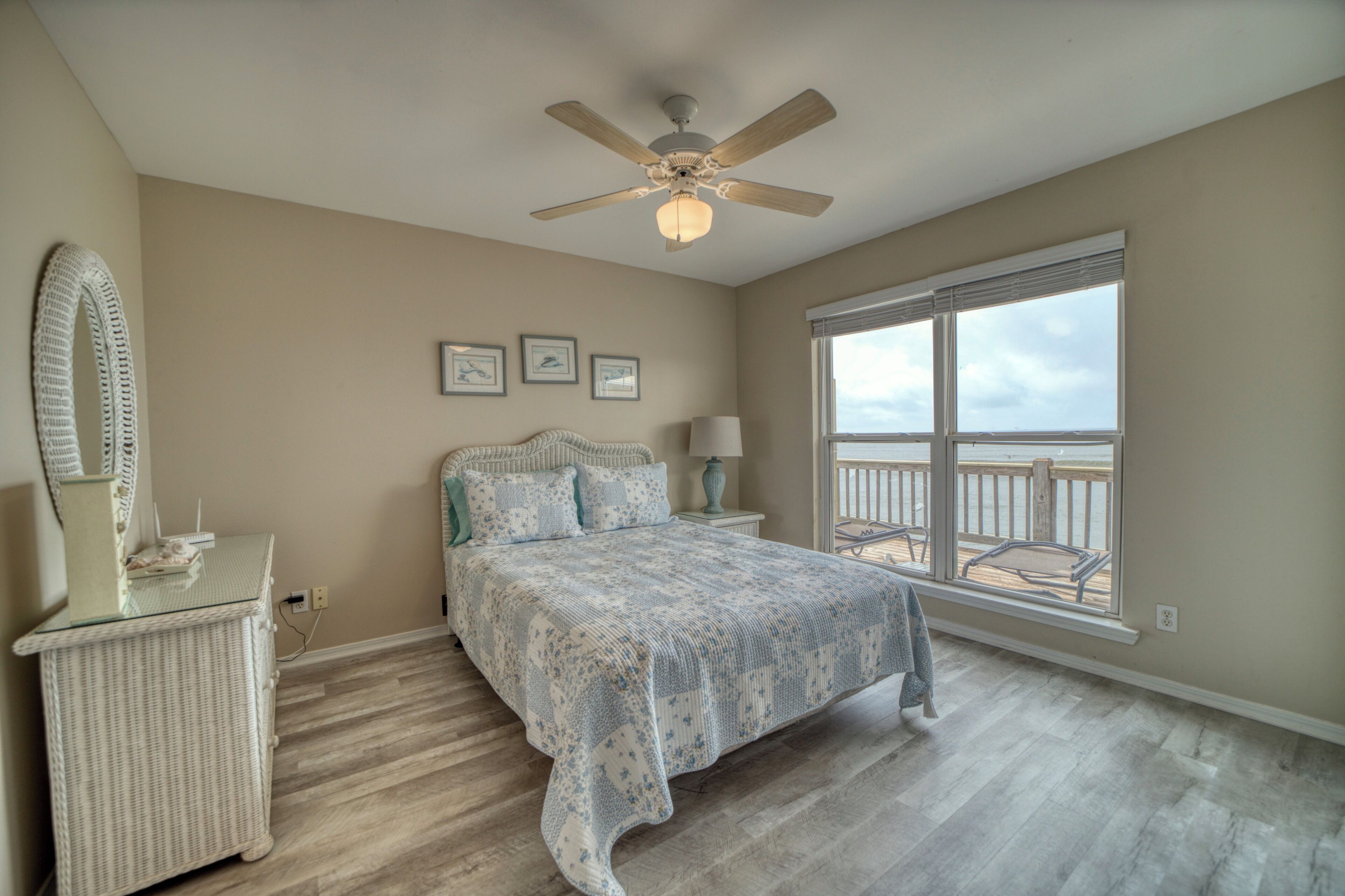 Une chambre à coucher comprenant un lit, un ventilateur de plafond, une fenêtre avec vue, une table de chevet et une commode.