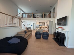 A spacious living area with a staircase leading to an upper level, a kitchen in the background, and a fireplace. - Newly constructed home in The Peninsula - 23708 Brickwalk ~ (Millsboro)