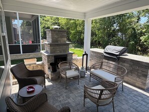 A covered patio with wicker furniture, a stone fireplace, and a barbecue grill. - Newly constructed home in The Peninsula - 23708 Brickwalk ~ (Millsboro)