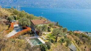 Ein Haus mit Schwimmbad, umgeben von Bäumen und Blick auf See und Berge.