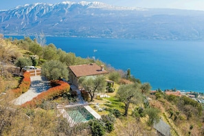 Ein Haus mit Schwimmbad, umgeben von Bäumen und Blick auf See und Berge.