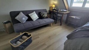 A room with a sofa, a small table with a lamp, a chair, a bed, and a trash bin. - Cosy apartment with 2 fully-equipped studios in Saint-Pierre-des-Corps, near train station (Saint-Pierre-des-Corps)
