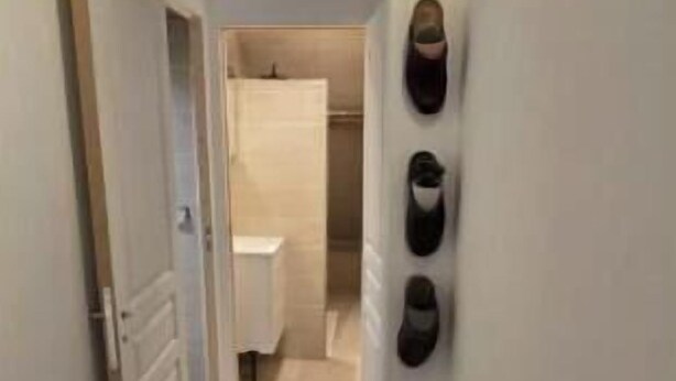 A narrow hallway with a wooden floor, a wall-mounted light fixture, and a door leading to a bathroom. - Cosy apartment with 2 fully-equipped studios in Saint-Pierre-des-Corps, near train station (Saint-Pierre-des-Corps)