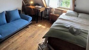A loft-style bedroom with a sloped ceiling, a bed, a blue sofa, a desk, and a window with a view of greenery. - Cosy apartment with 2 fully-equipped studios in Saint-Pierre-des-Corps, near train station (Saint-Pierre-des-Corps)