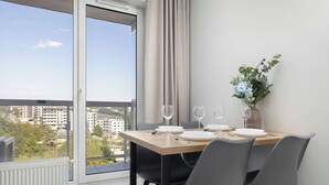 A dining area with a table set for four, a view of the city through a large window, and a potted plant on the windowsill. - Spacious Apartment with a Balcony | Parking (Lublin)