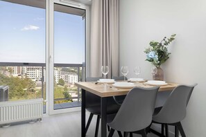 A dining area with a table set for four, a view of the city through a large window, and a potted plant on the windowsill. - Spacious Apartment with a Balcony | Parking (Lublin)