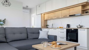 A modern kitchen with white cabinets, a built-in oven, and a dining area with a grey sofa and a wooden table. - Spacious Apartment with a Balcony | Parking (Lublin)