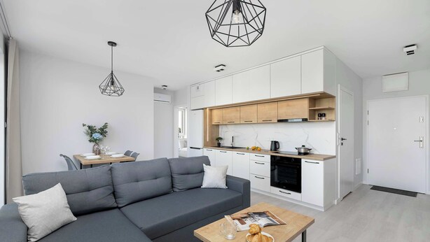 A modern living room with a grey sofa, a wooden coffee table, and a kitchen area with white cabinets and a wooden countertop. - Spacious Apartment with a Balcony | Parking (Lublin)