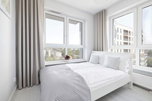A modern bedroom with a bed, large windows, and a view of buildings. - Spacious Apartment with a Balcony | Parking (Lublin)