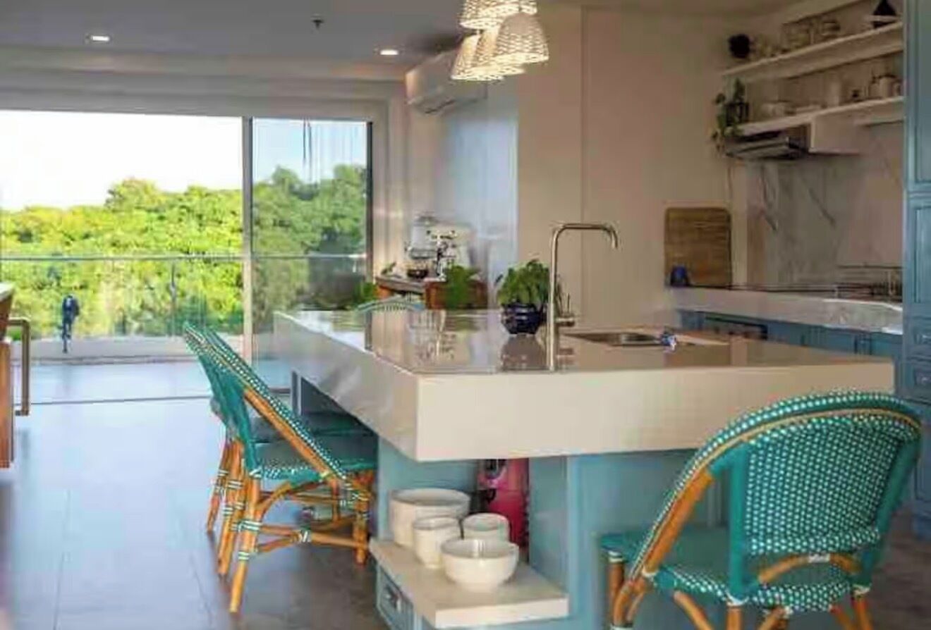 Une cuisine moderne dotée d’un grand îlot central, de tabourets de bar et offrant une vue sur la verdure environnante.