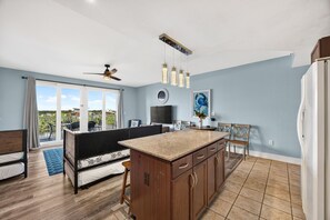 A modern kitchen with a central island, a dining area with chairs, a ceiling fan, and a large window with curtains. - Laketown Wharf 413 | Resort Pools, Walk to Beach, Sleeps 8 (Panama City Beach)