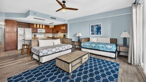Ein kleines Hotelzimmer mit einer Küchenzeile, zwei Betten, einem Deckenventilator und einem großen Fenster.