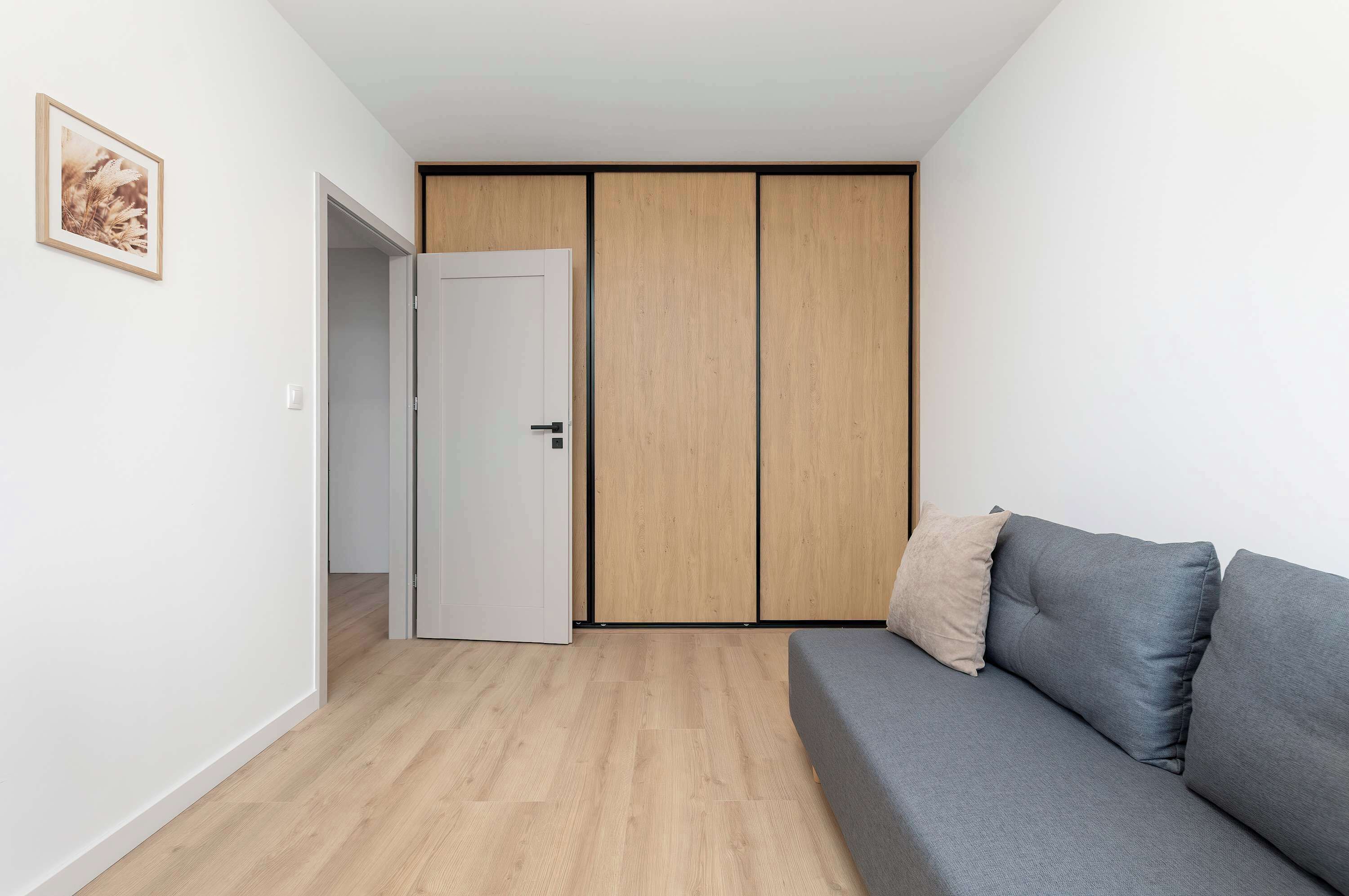 Una habitación moderna con un sofá gris, un armario de madera y una puerta blanca.