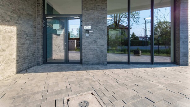 Entrada d'un edifici modern amb una porta de vidre, un piló de pedra i una zona pavimentada.