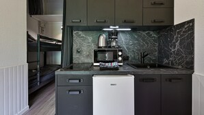Eine kompakte Küchenzeile mit Mikrowelle, Kaffeemaschine und kleinem Kühlschrank.