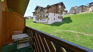 Ein Holz-Balkon mit Tisch und Bänken, mit Blick auf eine Rasenfläche vor mehrstöckigen Gebäuden.