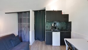 A compact kitchen with a microwave, coffee maker, and a small refrigerator. There is a dining table with a chair and a sofa with a cushion. - Modern Apartment in Manigod-La Clusaz with Mountain View, Shared Pool & Wi-Fi (Manigod)