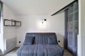 Un dormitorio moderno con un sofá gris, dos almohadas estampadas, una lámpara de pared y un radiador.