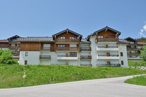 Un edificio de varios pisos con balcones, un camino pavimentado y una zona ajardinada.