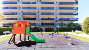A playground with a slide and swings, set against a multi-story building with balconies. - Family Apartments 2 Nova Pineda (La Pineda)