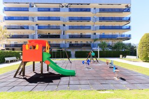 A playground with a slide and swings, set against a multi-story building with balconies. - Family Apartments 2 Nova Pineda (La Pineda)
